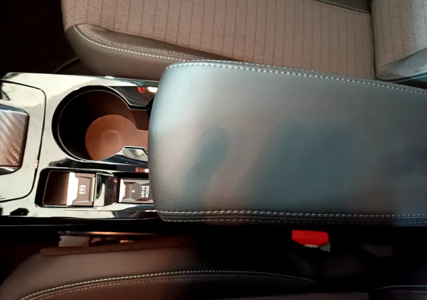 Gros plan sur la console centrale noire et accoudoir cuir gris foncé de la Peugeot 208 PureTech 2022, sièges tissu beige.