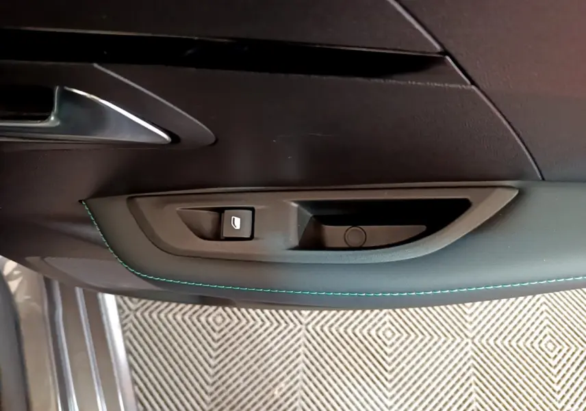 Gros plan sur la poignée intérieure de porte côté conducteur d'une Peugeot 208 gris foncé avec surpiqûres bleues.