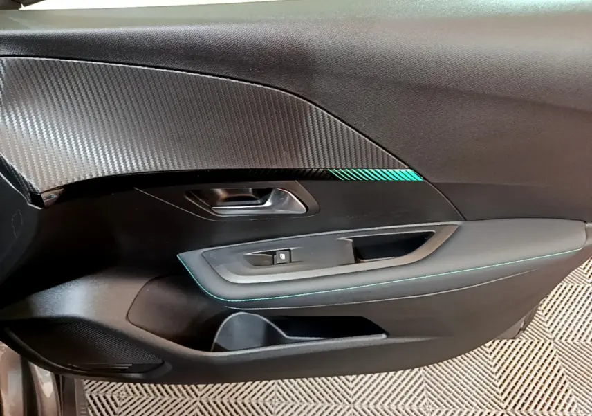 Gros plan sur la porte intérieure côté gauche de la Peugeot 208 gris foncé avec surpiqûres bleues et insert décoratif.