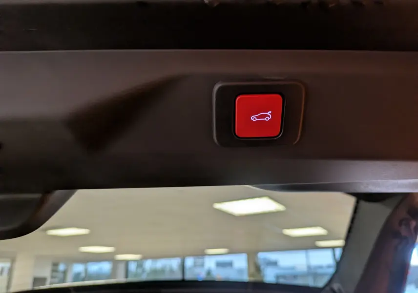 Bouton rouge d'ouverture électrique du hayon, visible sur le bord intérieur du coffre du Peugeot 3008 gris titane toit noir.