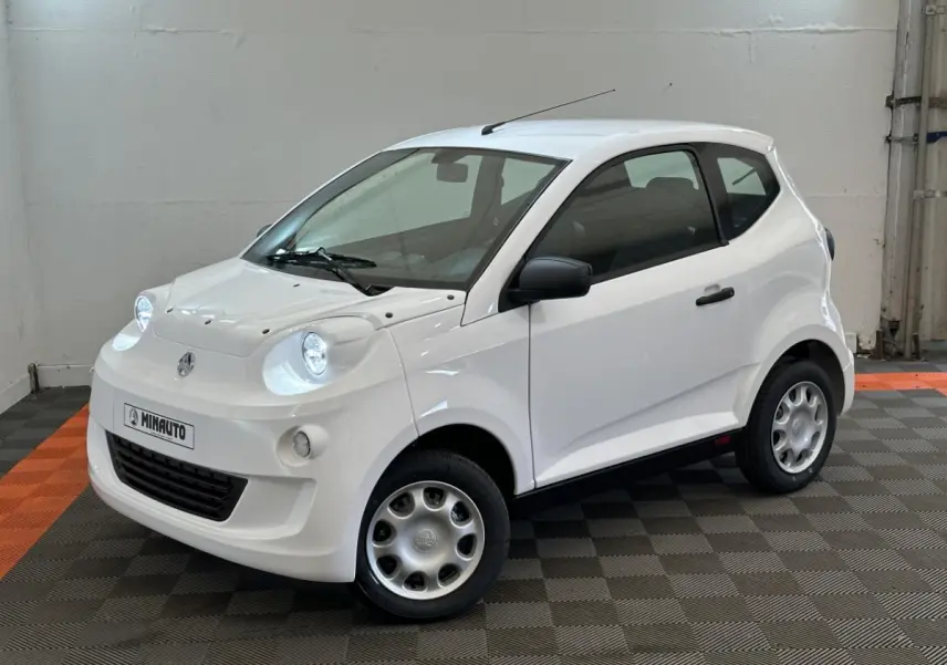 Vue 3/4 avant d'une Aixam Minauto E Access blanche avec rétroviseur caméra côté gauche dans un intérieur neutre.