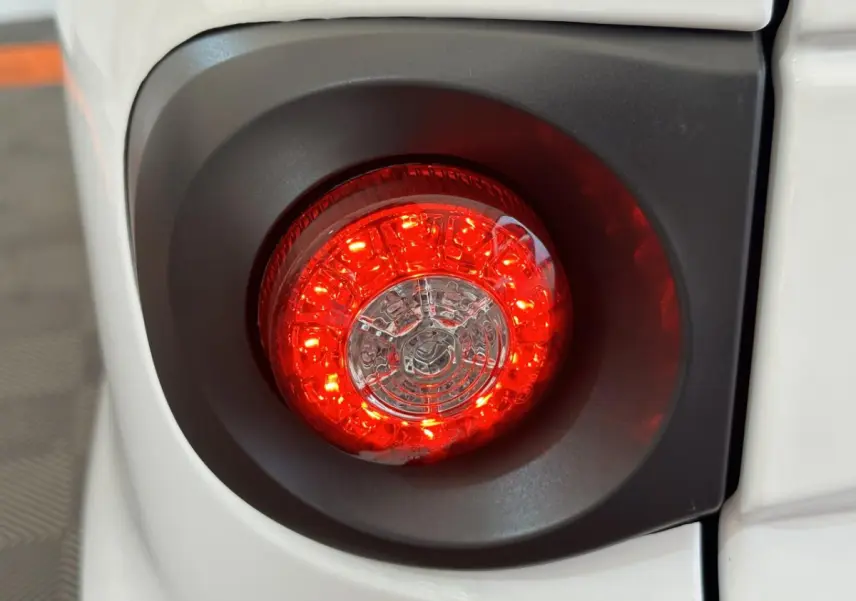 Gros plan sur le feu arrière rouge circulaire du côté gauche de l'AIXAM MINAUTO E ACCESS blanc 2025 électrique.