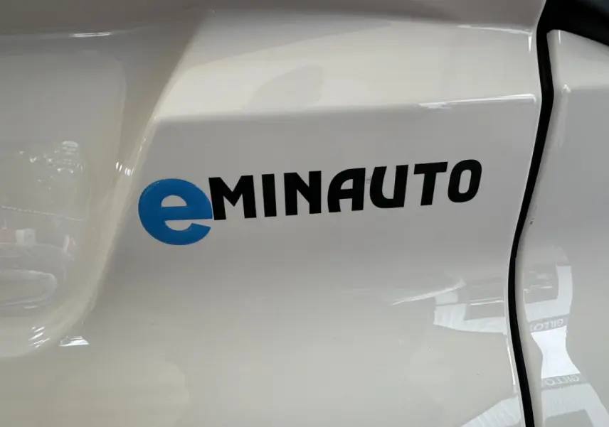 Gros plan sur le logo eMINAUTO bleu et noir sur la portière blanche côté conducteur d'une Aixam MINAUTO E ACCESS 2025 électrique.