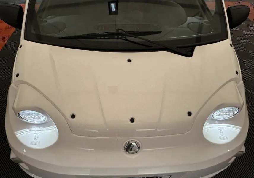 Vue plongeante sur l'avant blanc de l'AIXAM MINAUTO E ACCESS 2025 avec phares ovales et logo central visible.