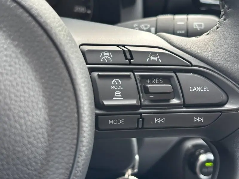 Gros plan sur les commandes du volant multifonction noir de la Toyota Yaris blanche 2025, avec régulateur adaptatif et aide au maintien de trajectoire.