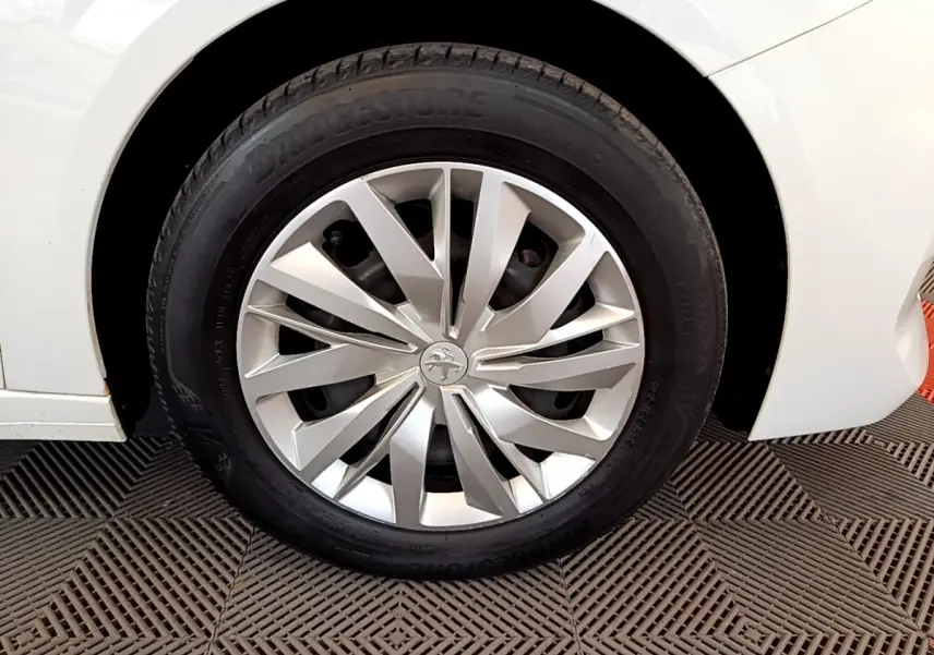 Gros plan sur la roue avant gauche d'une Peugeot 208 blanche, mettant en valeur la jante en alliage au design moderne.