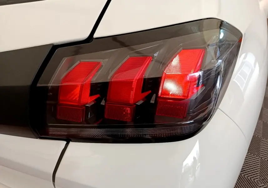 Gros plan sur le feu arrière droit rouge et noir d'une Peugeot 208 blanche, soulignant les lignes anguleuses du design.