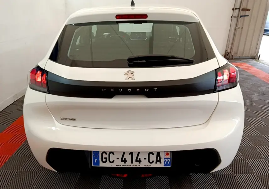 Vue arrière d'une Peugeot 208 blanche avec bande noire distinctive et feux arrière allumés en intérieur.