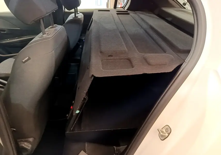 Vue intérieure arrière droite de la Peugeot 208 blanche, montrant la cloison pleine et les sièges noirs.