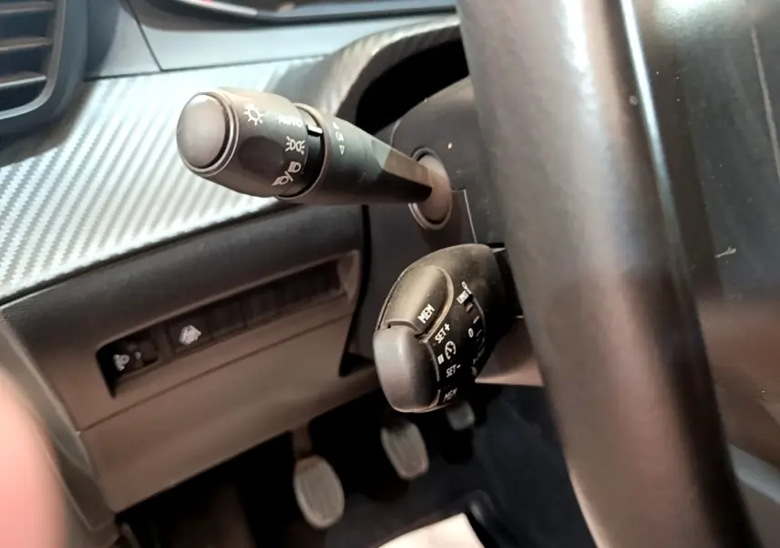 Gros plan sur la colonne de direction et commandes du volant d’une Peugeot 208 blanche, version essence 2021.