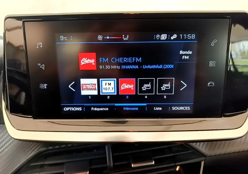 Écran tactile central affichant la radio FM dans l'habitacle d'une Peugeot 208 blanche, vue de face.