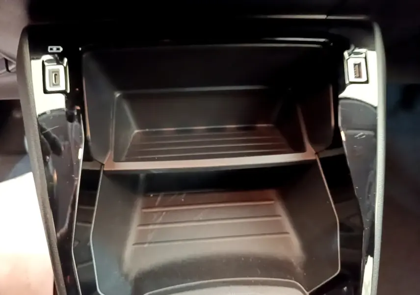 Gros plan sur le rangement central noir de la Peugeot 208 1.2 PT 75 S&S Premium, avec ports USB visibles.