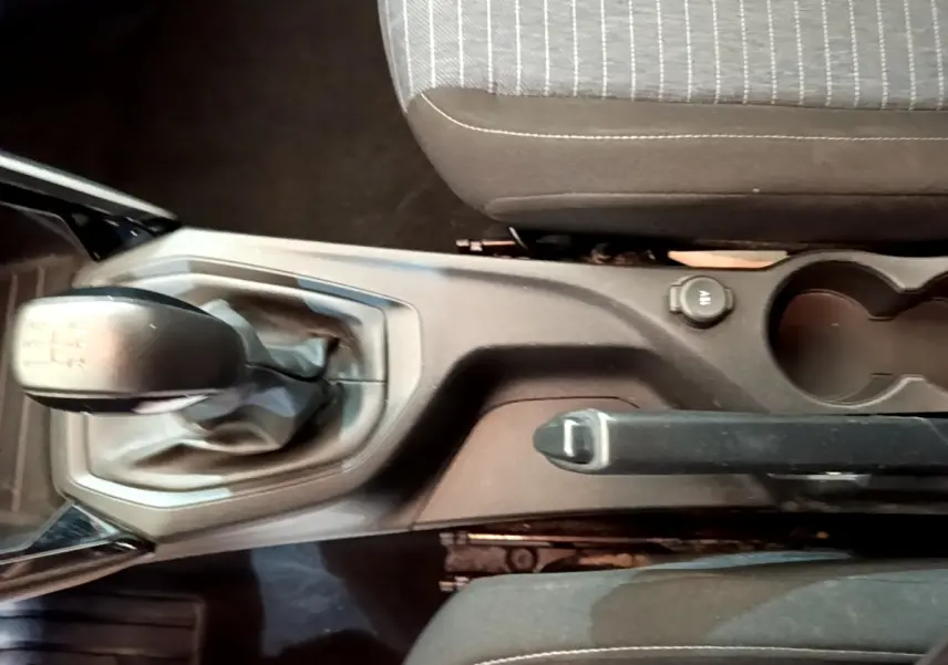 Vue plongeante sur la console centrale noire d'une Peugeot 208 blanche, avec levier de vitesse manuel et frein à main.