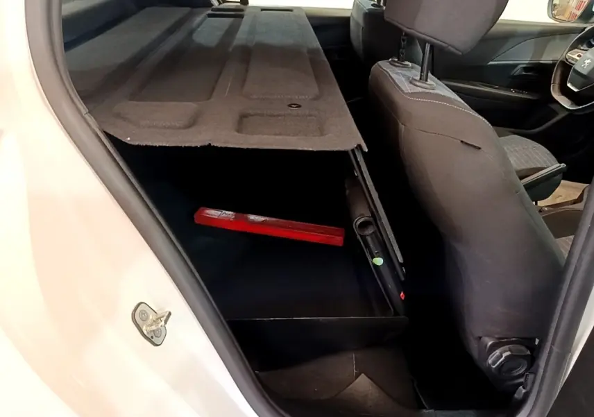 Vue intérieure côté gauche du coffre ouvert d'une Peugeot 208 blanche avec banquette arrière et siège avant en tissu gris.