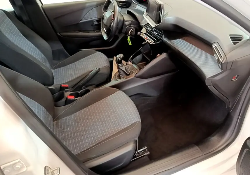 Intérieur de la Peugeot 208 blanc vue côté conducteur, montrant sièges tissu gris et tableau de bord moderne.