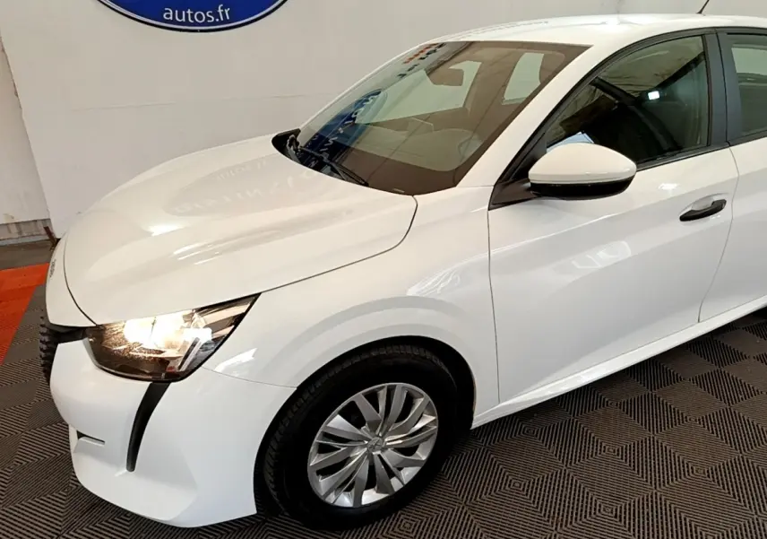 PEUGEOT 208 blanc vue 3/4 avant droit avec phares allumés et jantes alliage au sol texturé.