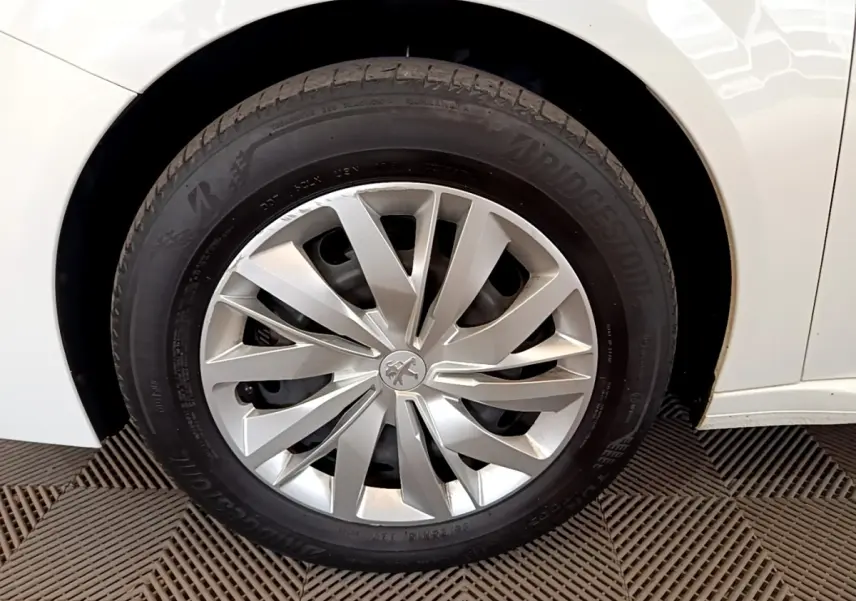 Gros plan sur la roue avant droite d'une Peugeot 208 blanche, mettant en valeur la jante argentée au design moderne.
