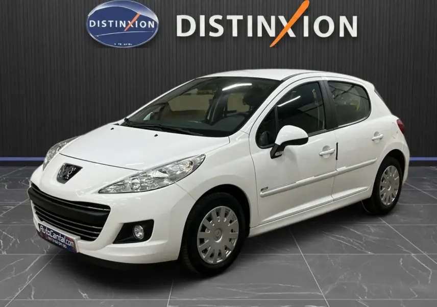 Peugeot 207 blanche vue 3/4 avant droit, avec calandre et baguettes de porte chromées, en intérieur showroom.