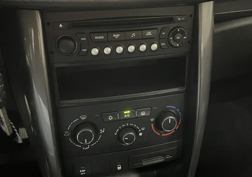 Vue rapprochée du tableau de bord central noir de la Peugeot 207 Active 2011 avec commandes climatisation et radio.