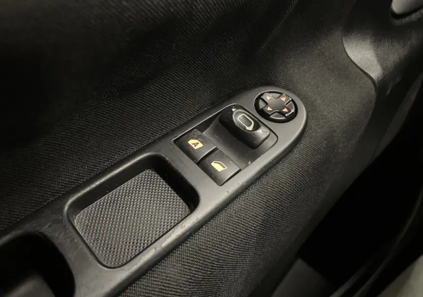 Gros plan sur les commandes de lève-vitres et réglage des rétroviseurs côté conducteur d’une Peugeot 207 blanche de 2011.