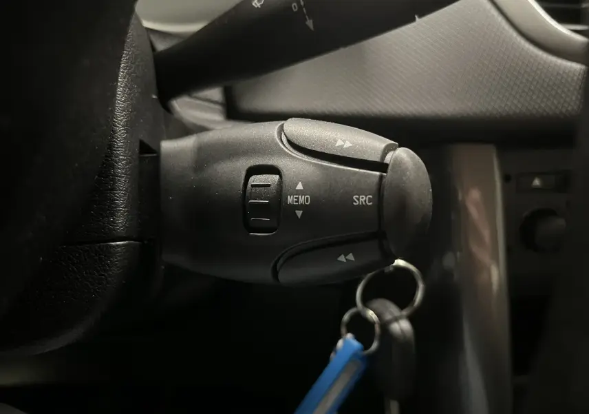 Gros plan sur la commande au volant côté gauche de la Peugeot 207 Active 2011, avec clé et intérieur gris noir visible.