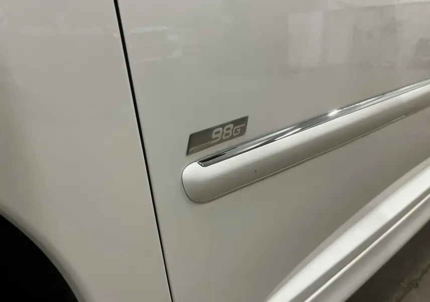 Gros plan sur la porte côté gauche d'une Peugeot 207 blanche avec badge finition 98G et baguette chromée.