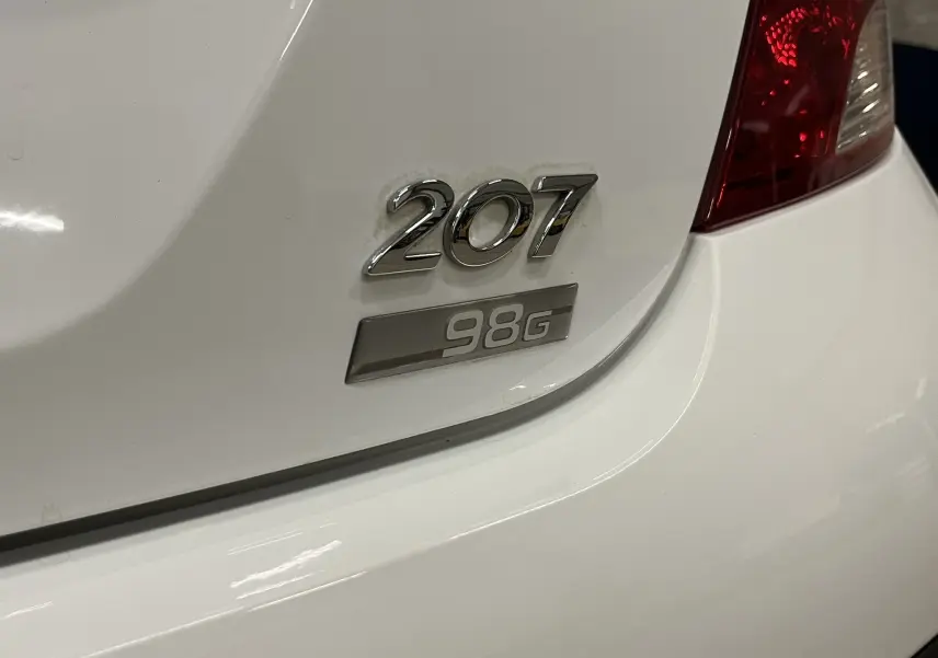 Gros plan sur l'arrière droit blanc d'une Peugeot 207 avec le logo 207 et l'insigne finition 98G visible.