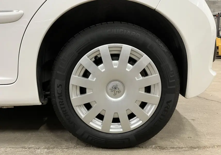 Gros plan sur la roue avant droite blanche d'une Peugeot 207 Active 2011 avec enjoliveur argenté et logo lion.