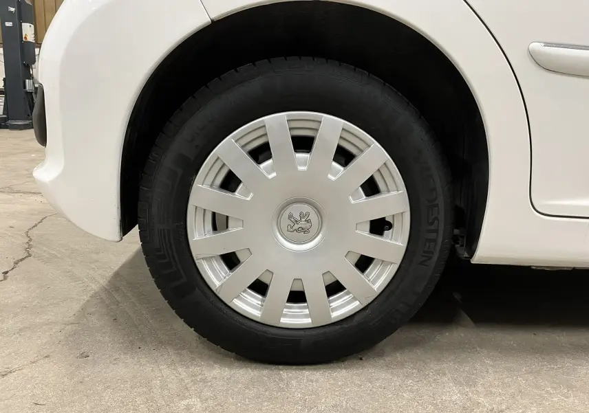 Gros plan sur la roue avant gauche blanche d'une Peugeot 207 Active 2011 avec enjoliveur argenté et logo lion central.