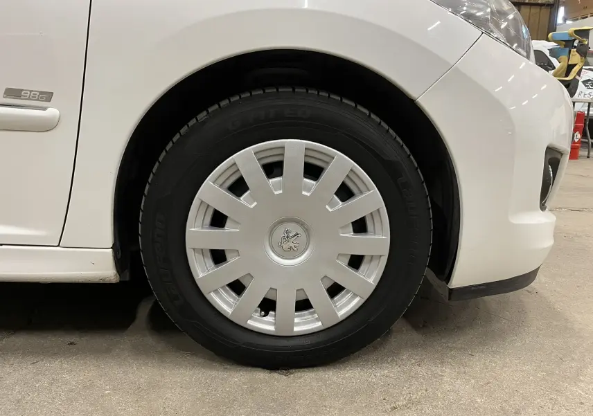 Gros plan sur la roue avant droite blanche d'une Peugeot 207 Active 1.6 HDI avec enjoliveur et badge lion au centre.
