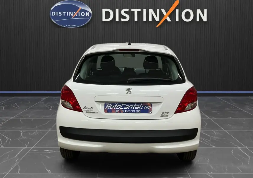 Vue arrière d'une Peugeot 207 blanche finition Active, avec calandre et baguette de porte chromées visibles.
