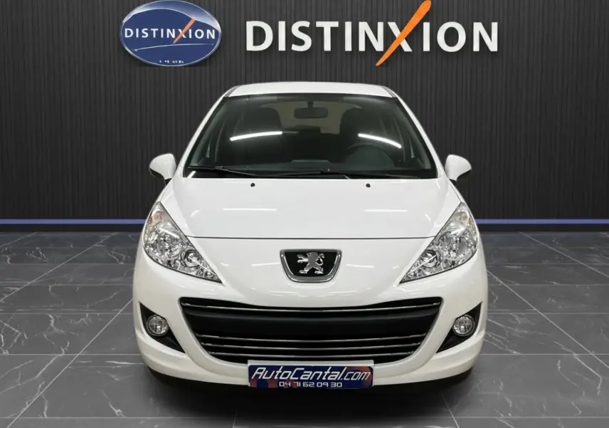 Peugeot 207 blanche vue de face, calandre et phares distinctifs, dans un showroom avec logo Distinxion en arrière-plan.