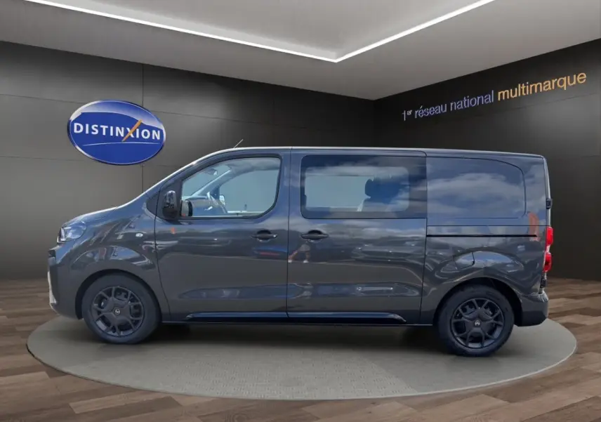 Profil droit d’un Citroën Jumpy gris foncé 2026 avec vitres latérales et jantes noires en showroom.