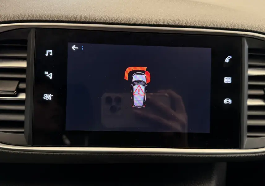 Écran tactile central de la Peugeot 308 blanc montrant une alerte de capteurs de stationnement avant.