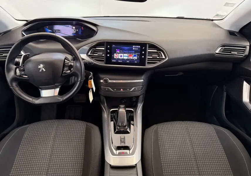 Intérieur de la Peugeot 308 2021 vue de face, tableau de bord noir avec écran tactile central et volant cuir.