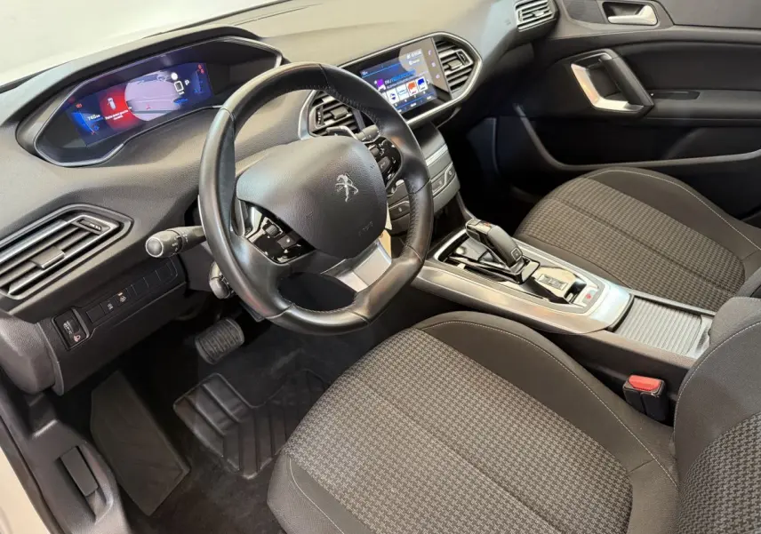 Intérieur de la Peugeot 308 2021 vu côté conducteur, volant cuir, écran tactile et sièges tissu gris à motifs.