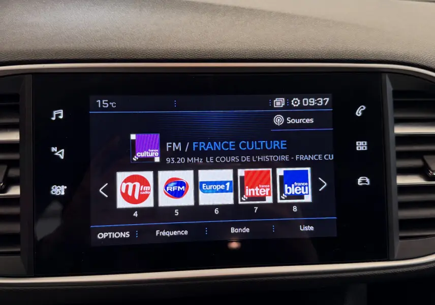 Écran tactile central du tableau de bord de la Peugeot 308 blanc, affichant les stations radio FM.