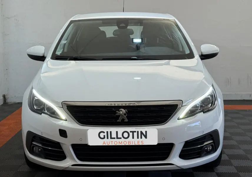 Vue frontale d'une Peugeot 308 blanche avec feux LED allumés et logo lion visible sur la calandre.