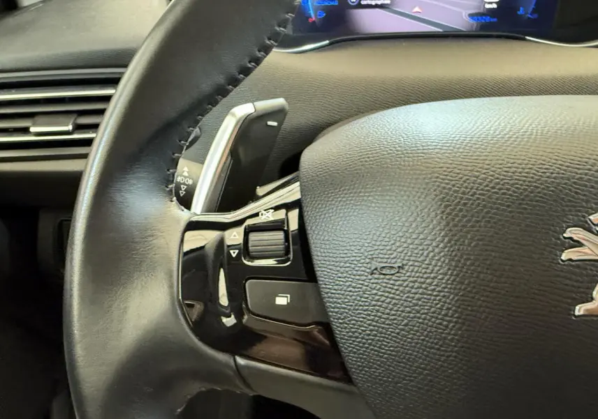 Gros plan sur le volant cuir noir de la Peugeot 308 2021 avec commandes intégrées et tableau de bord numérique visible.