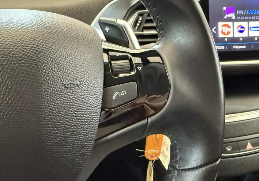 Gros plan sur le volant cuir noir côté gauche du Peugeot 308 2021 avec commandes et écran tactile en arrière-plan.