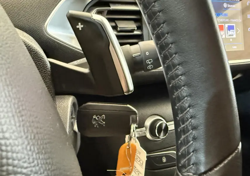 Gros plan sur le volant cuir noir et la clé Peugeot insérée dans le contact d'une 308 blanche, tableau de bord en arrière-plan.