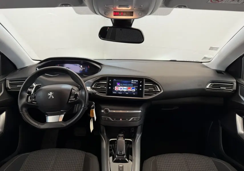 Vue frontale de l'intérieur noir de la Peugeot 308 2021 avec volant cuir, écran tactile central et tableau de bord digital.