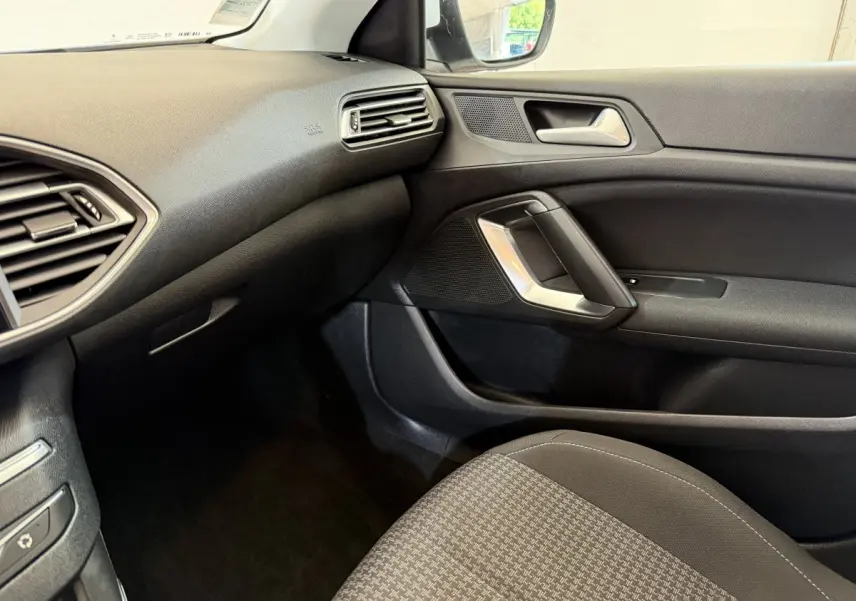 Vue intérieure côté passager de la Peugeot 308 blanche, mettant en valeur la porte et le tableau de bord noir.