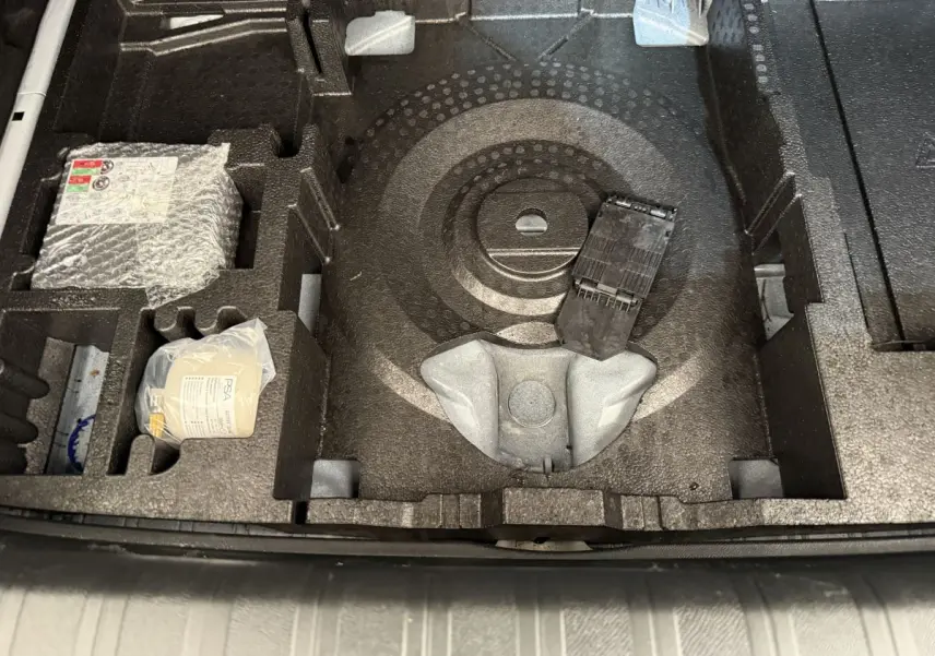 Vue plongeante sur le compartiment de rangement sous le plancher du coffre d'une Peugeot 308 blanche, avec accessoires intégrés.