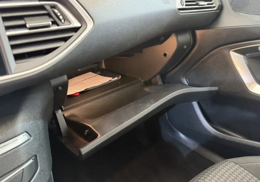 Gros plan sur la boîte à gants ouverte côté passager du Peugeot 308 2021, intérieur noir avec documents visibles.