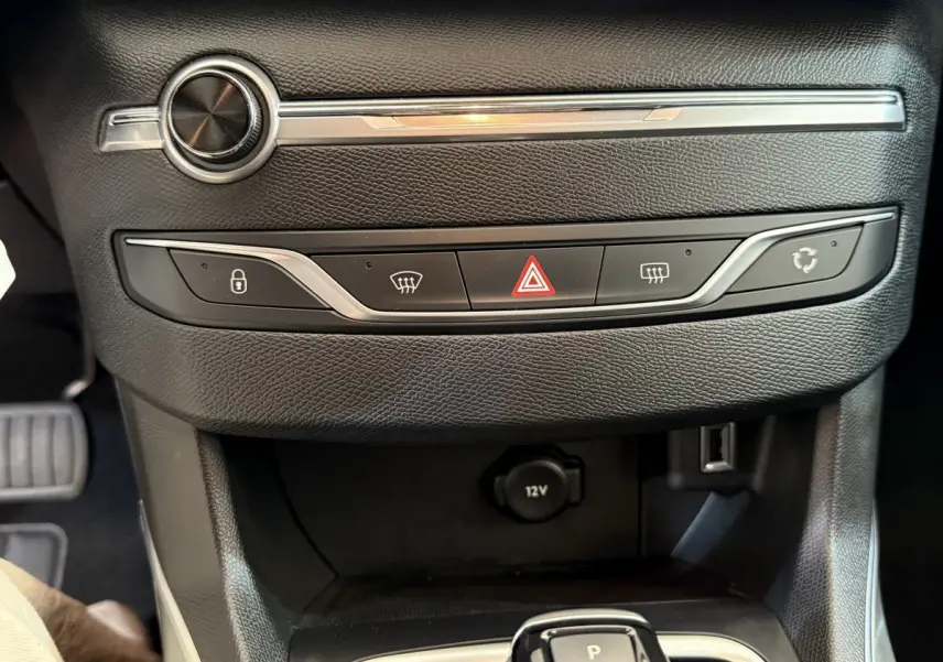 Gros plan sur la console centrale noire de la Peugeot 308 avec boutons de verrouillage, hazard et prise 12V visible.