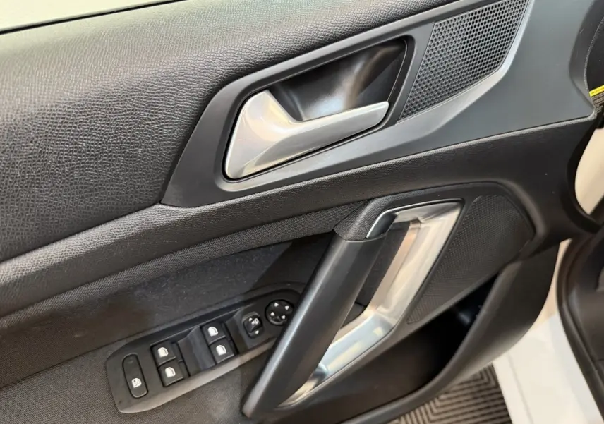 Gros plan sur la porte côté conducteur de la Peugeot 308 blanche, montrant la poignée argentée et les commandes des vitres.