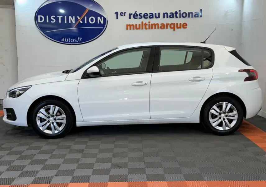 Profil droit d'une Peugeot 308 blanche de 2021, version BlueHDi 130 EAT8 Active Business, en intérieur showroom.
