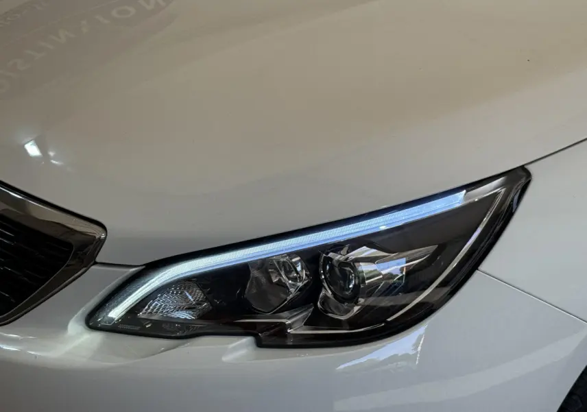 Gros plan sur le phare avant droit à LED d'une Peugeot 308 blanche, mettant en valeur son design moderne.