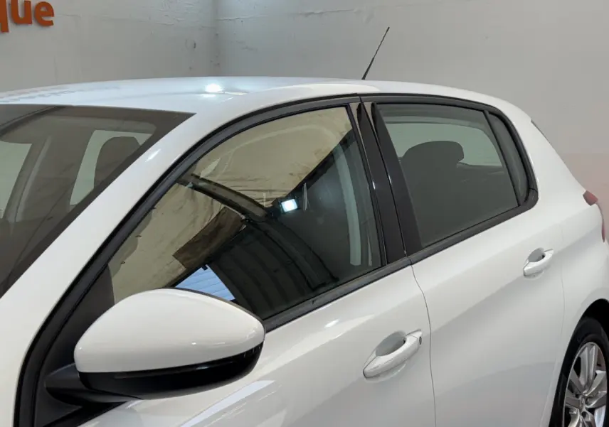 Vue latérale côté gauche d'une Peugeot 308 blanche, mettant en valeur les vitres teintées et les rétroviseurs blancs.